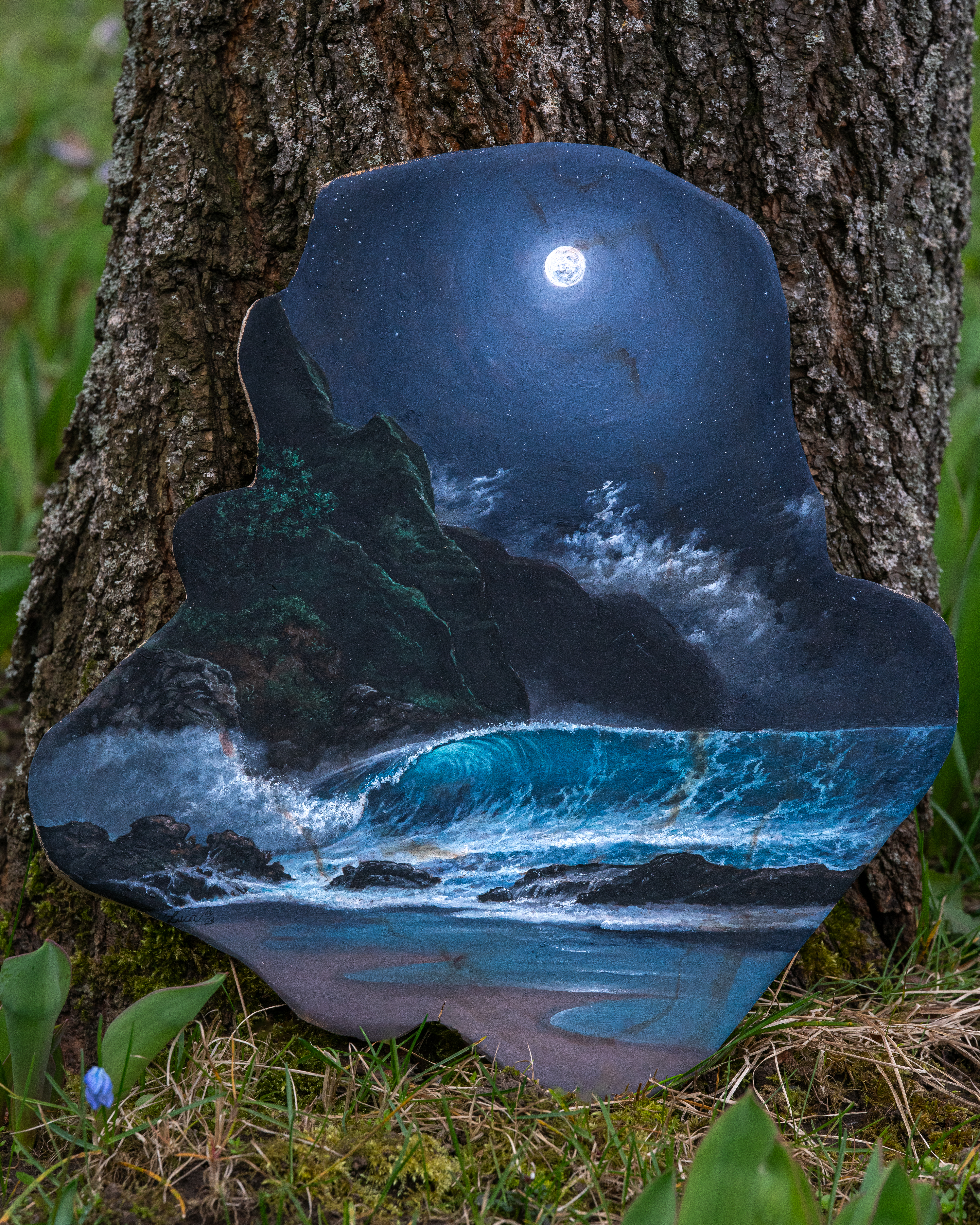 Eine Strandszenerie bei Nacht. Eine große Welle bricht sich gerade an der felsigen Küste. Darüber steht der Vollmond